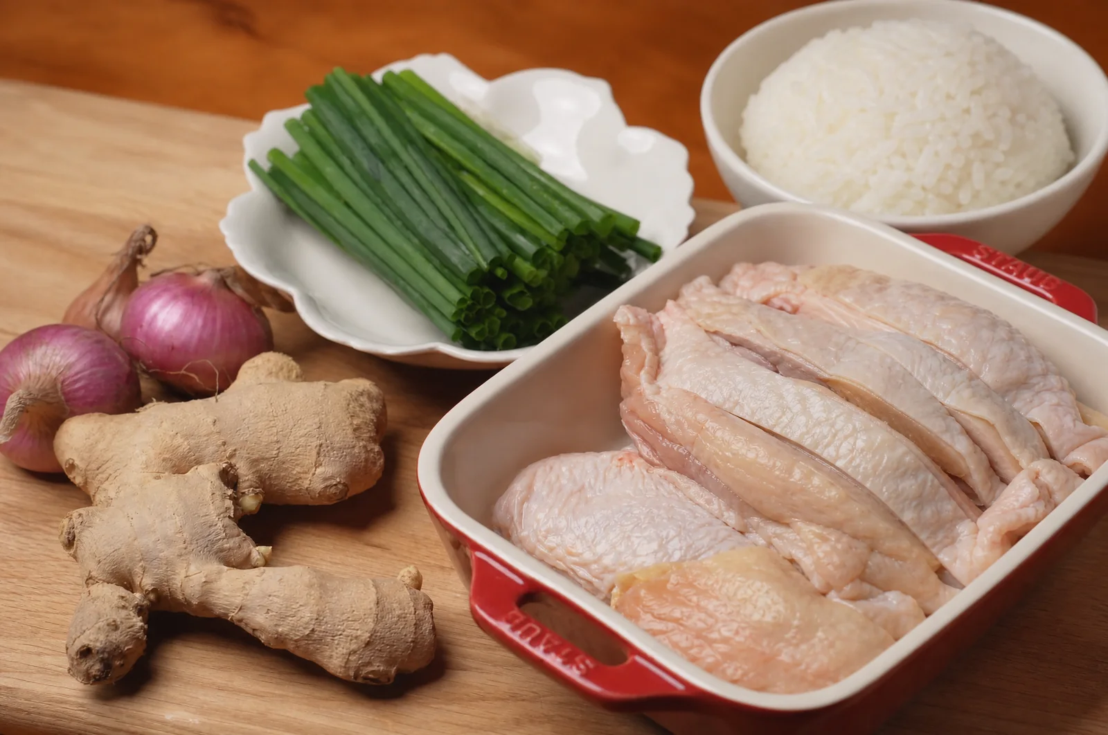 Chicken, jasmine rice, ginger, scallions, shallots, and other ingredients arranged on a table