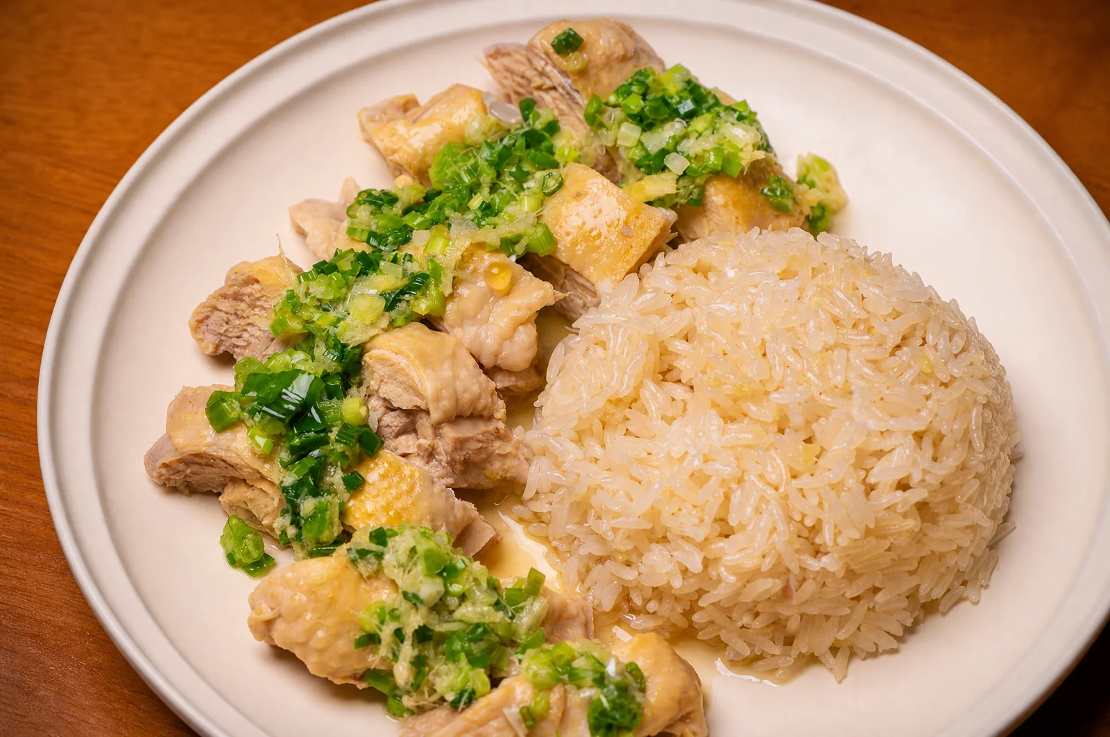 A plated serving of sliced Hainanese chicken with fragrant rice and ginger-scallion sauce