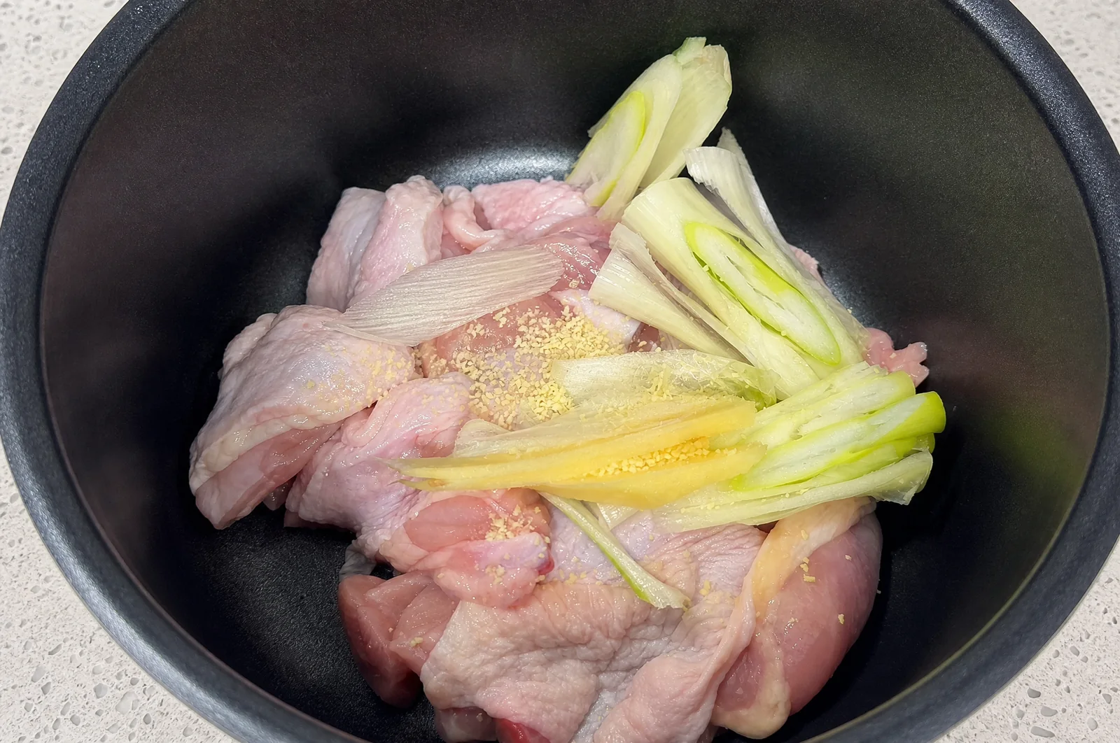 Raw chicken pieces with ginger and scallions arranged in a cooking pot